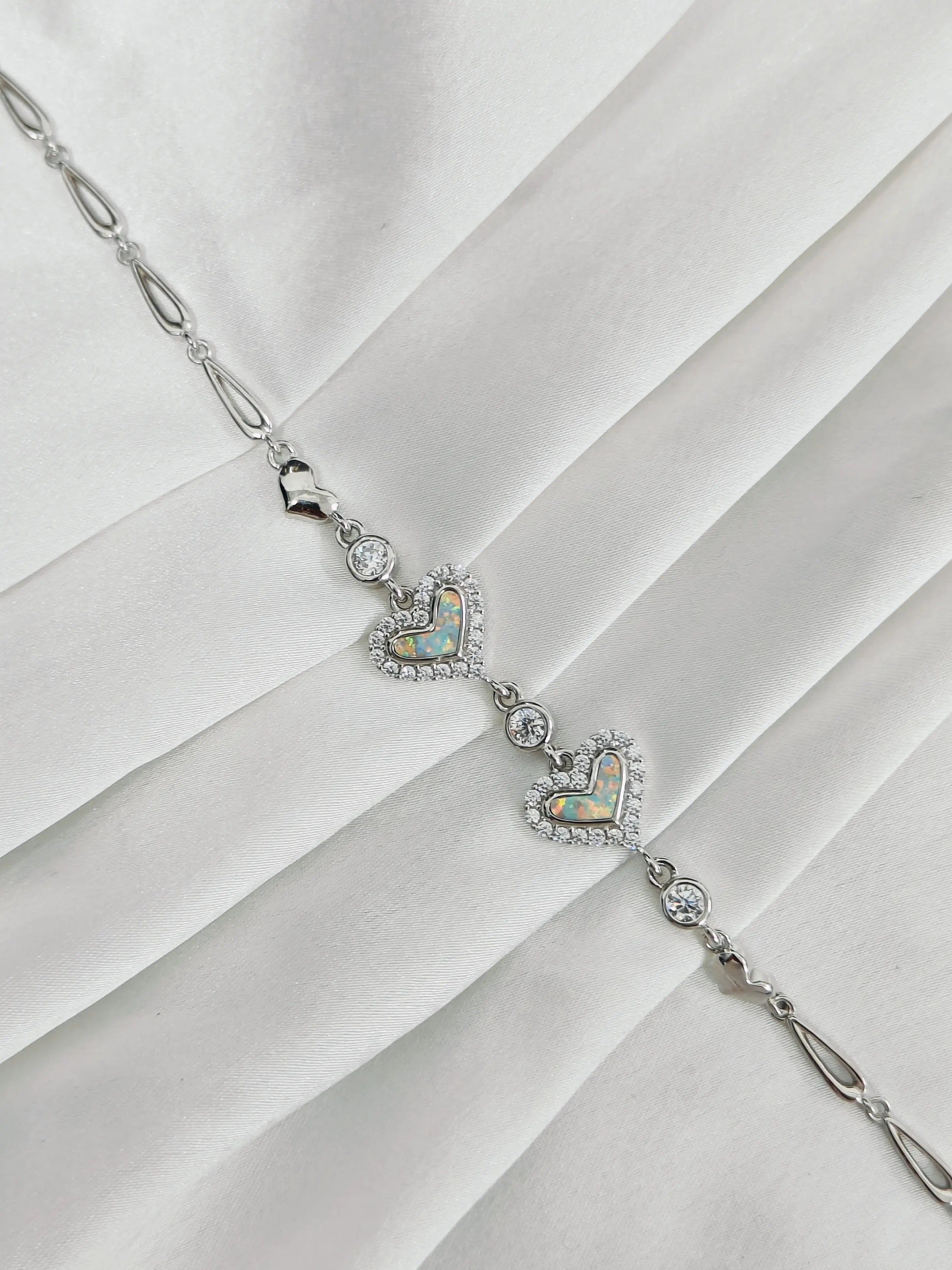 Silver necklace with heart-shaped opalite pendants on a white fabric background